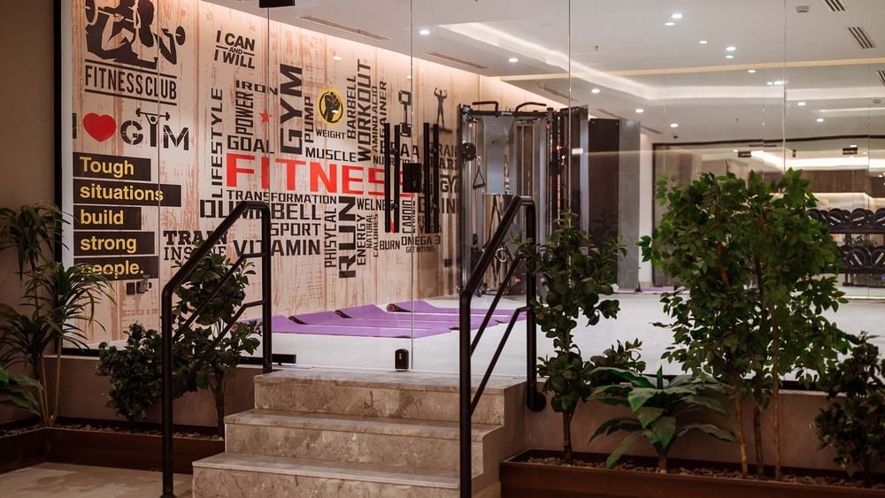 Marble stairs by green plants leading to a gym with yoga mats under a typographic wall at Cantonal Hotel by Warwick Riyadh