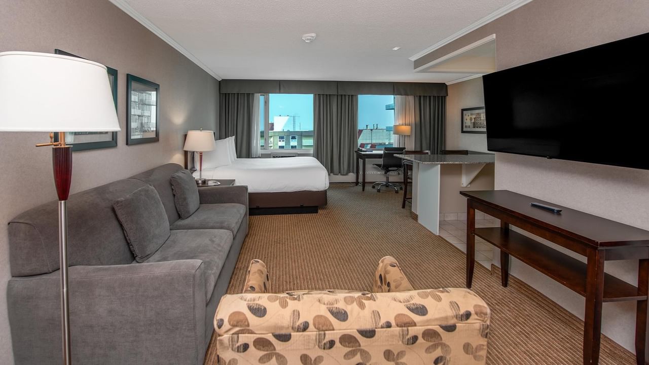Spacious hotel suite with a sofa, armchair, king bed, dining table and wall-mounted TV.