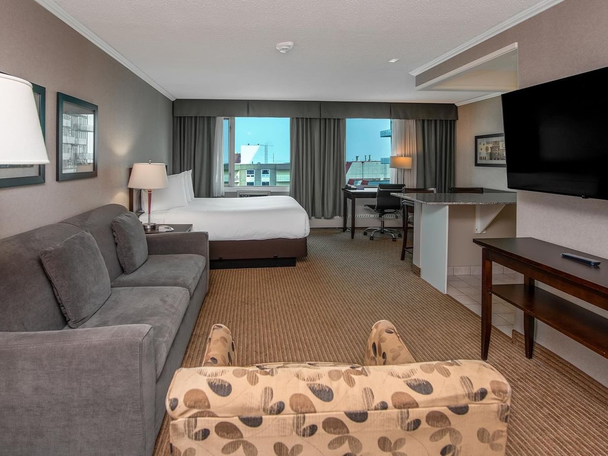 Spacious hotel suite with a sofa, armchair, dining table and wall-mounted TV.