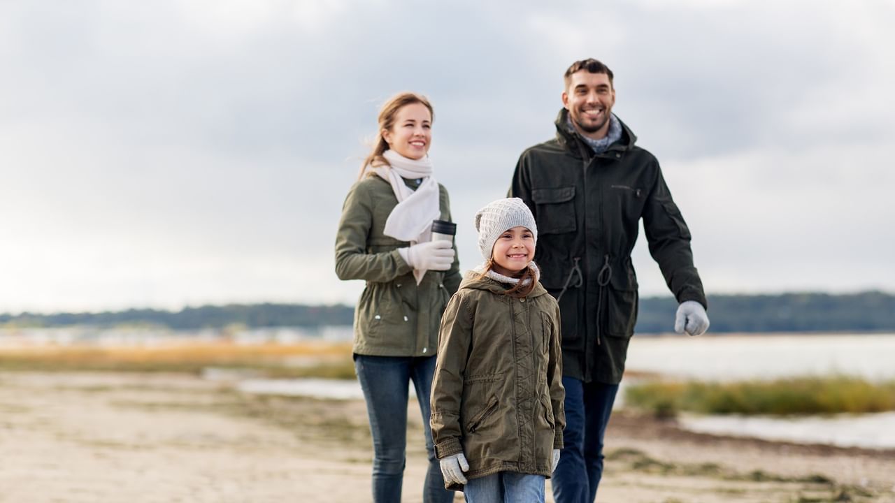 A family of three, dressed warmly, walks together on a beach path.