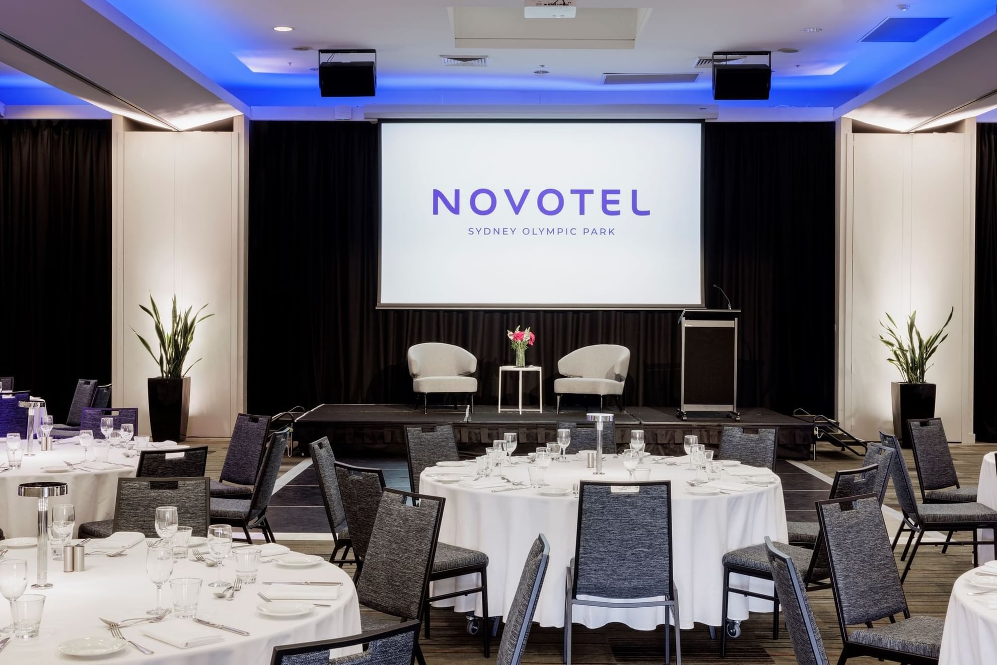 A elegantly set dining table on the Freshwater Balcony at Novotel Sydney Olympic Park, adorned with flowers & fine cutlery