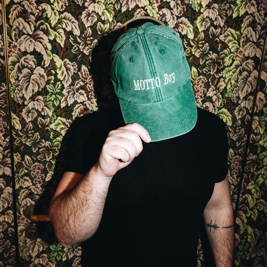 Mann mit Motto Boy Kappe vor floralem Hintergrund im Hotel Motto Wien