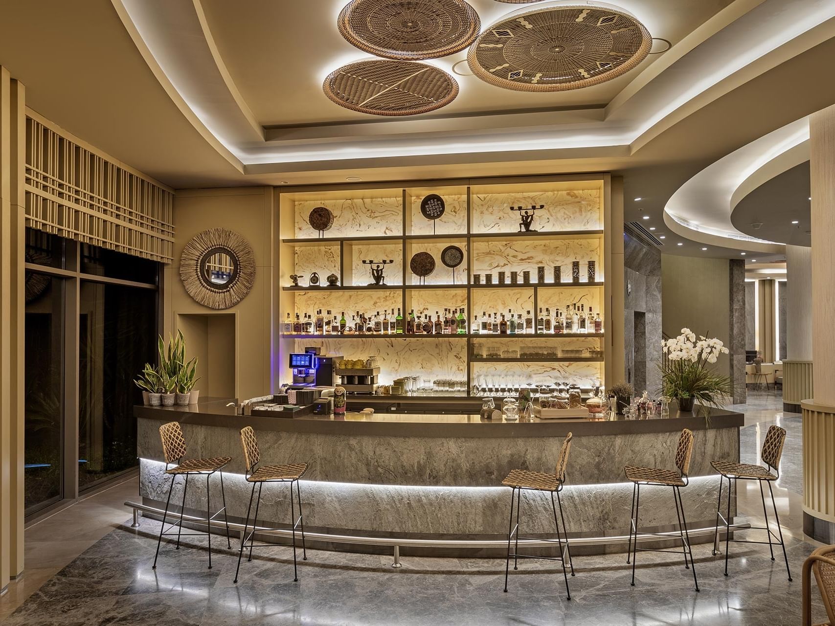Elegant bar interior at Titanic Luxury Collection Bodrum, featuring stylish chairs, liquor shelves, and floral décor.