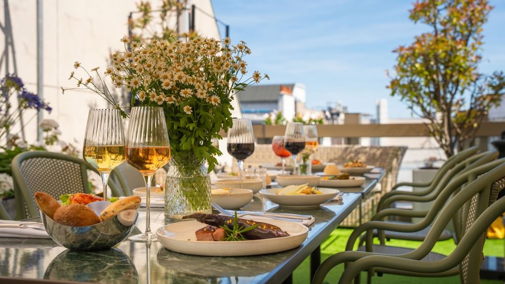 Table dressée avec plats gastronomiques et verres de vin sur la Terrasse Le W au Warwick Paris Champs-Elysées