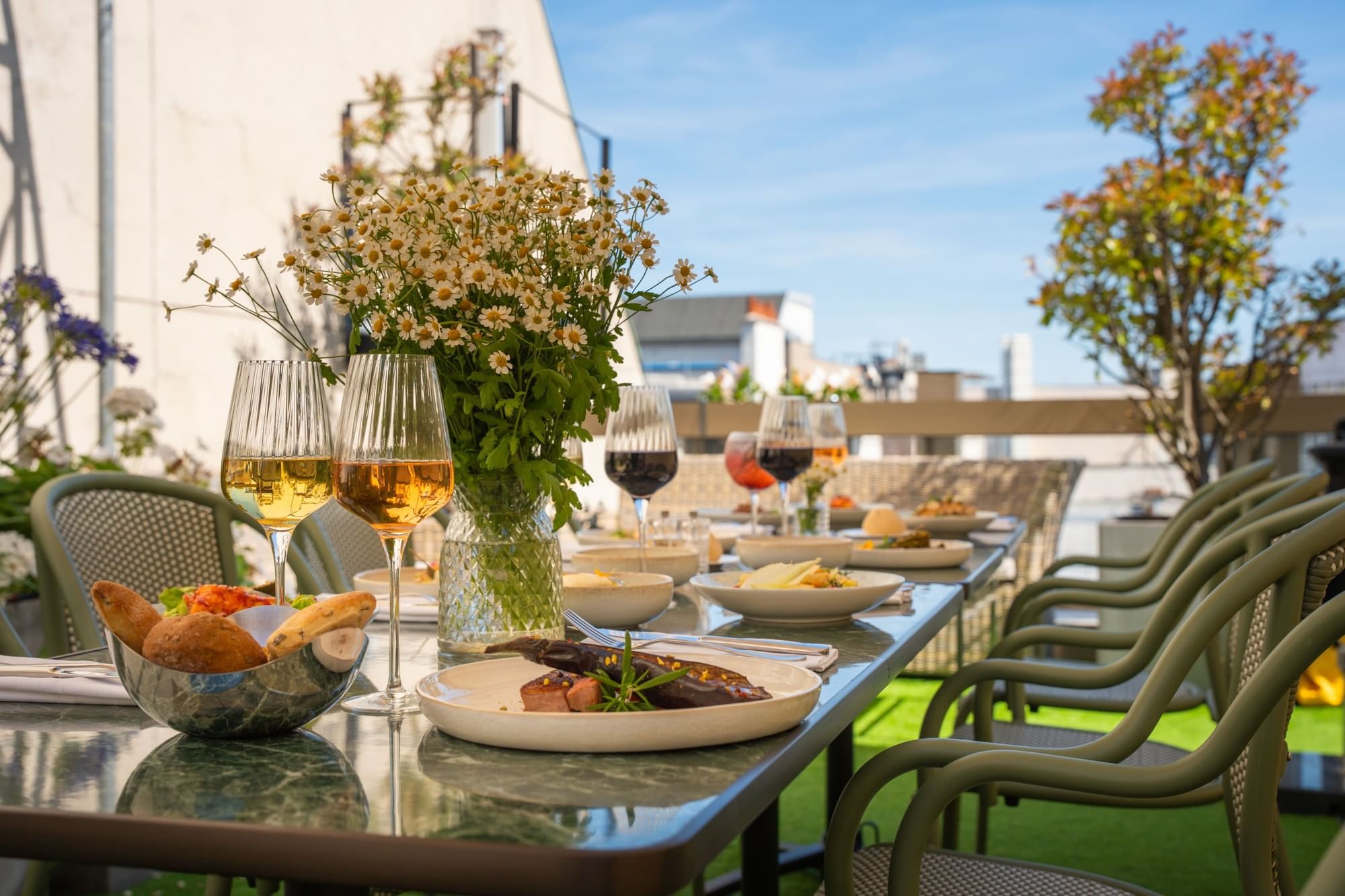 A beautifully set outdoor dining table with food, wine glasses, and flowers.
