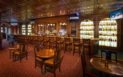 Bar at The Stanley Hotel, with a long wooden bar, a red patterned carpet, and shelves of liquor with ambient lighting