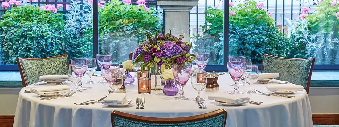 Dining table set with glasses & floral arrangements by window in Eaton Suite at The Capital Hotel, Apartments and Townhouse