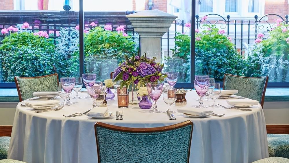 Dining table set with glasses & floral arrangements by window in Eaton Suite at The Capital Hotel, Apartments and Townhouse