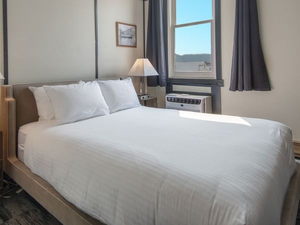 Hotel room with queen bed, night stand, lamp, and window