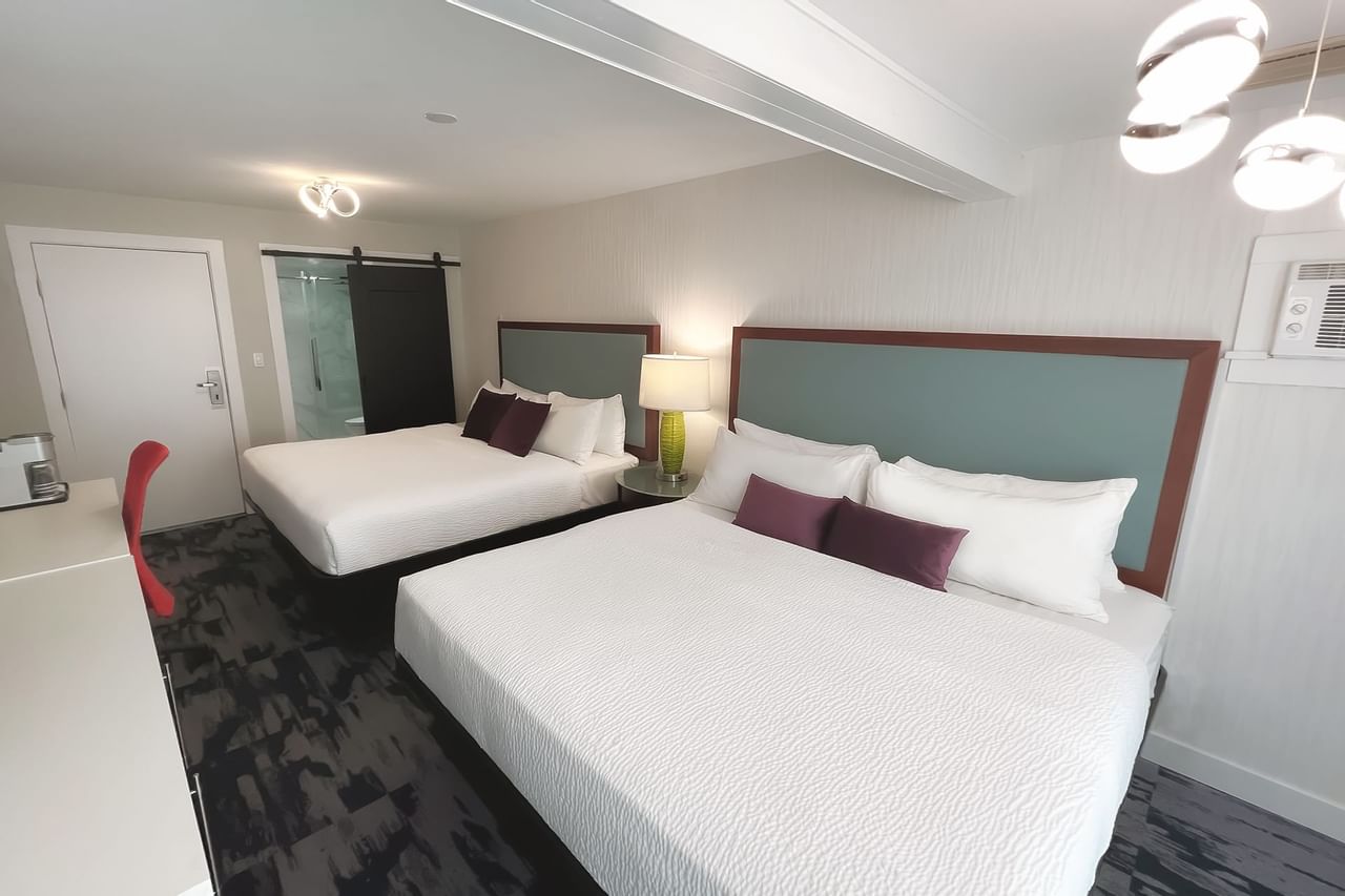 Guest room with two king beds, pillows, a desk, chair and toilet