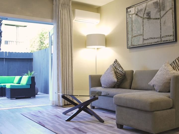 A wide view of a living room with a sofa, coffee table, lamp, and artwork, showing a sliding door to an outdoor area.