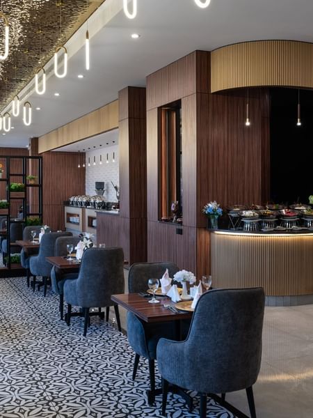 Blue chairs by wooden tables surrounding a patterned floor under oval lights in KVNT at Warwick Al Jubail
