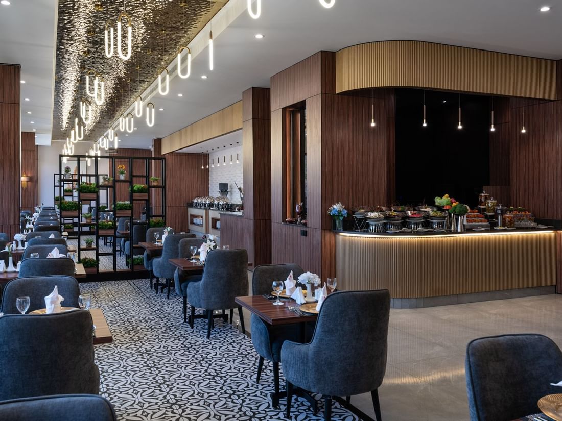 Blue chairs by wooden tables surrounding a patterned floor under oval lights in KVNT at Warwick Al Jubail