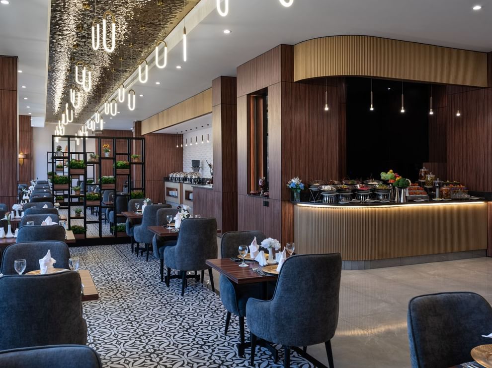 Blue chairs by wooden tables surrounding a patterned floor under oval lights in KVNT at Warwick Al Jubail