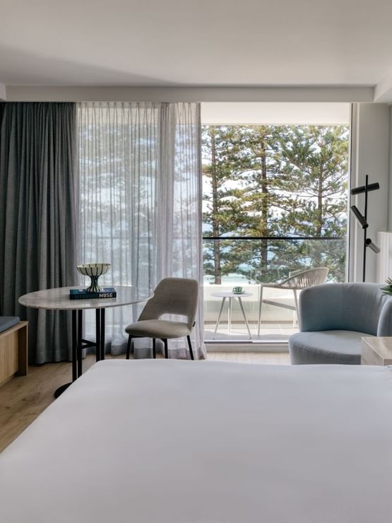 Ocean View King at Elysium Manly featuring a lounge chair and table by large windows surrounding a bed