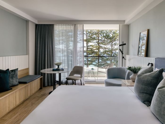 Ocean View King at Elysium Manly featuring a lounge chair and table by large windows surrounding a bed