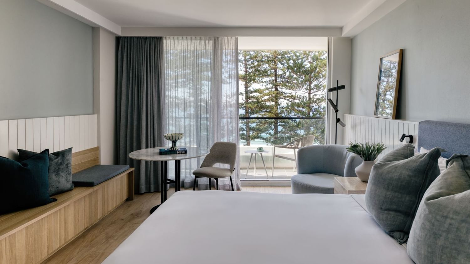 Ocean View King at Elysium Manly featuring a lounge chair and table by large windows surrounding a bed