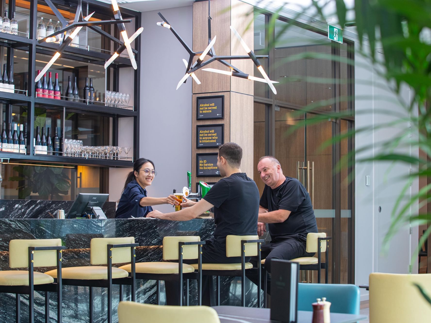 Three people at a bar, one is a bartender, the other two are seated customers.