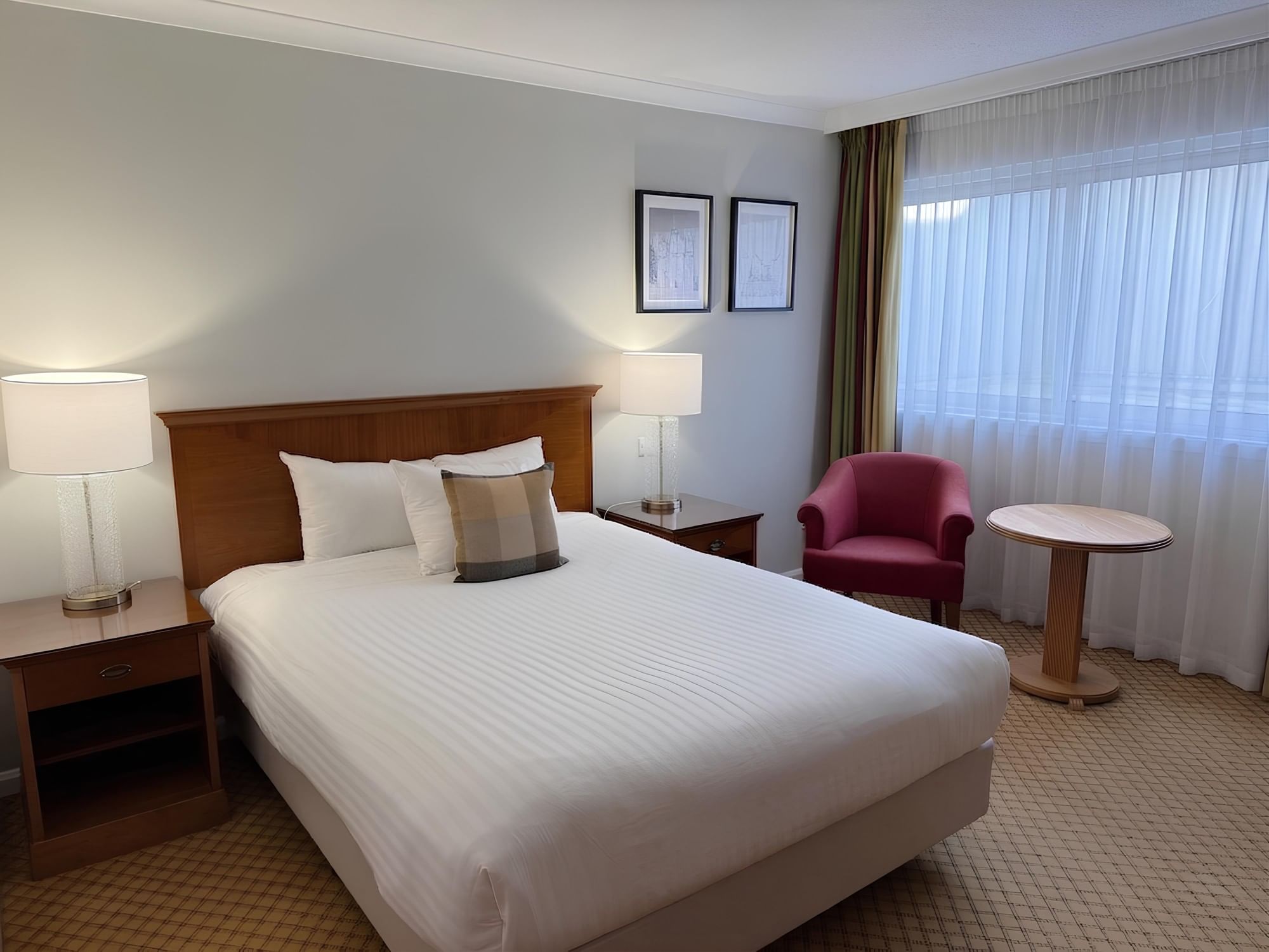 Standard double room at Aberdeen Dyce Hotel featuring a comfortable bed, red armchair, and work table by the window.