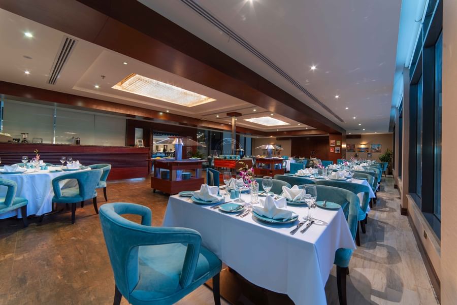 Italian restaurant interior with teal armchairs by tables with white cloths and orchids at Warwick Al Khobar