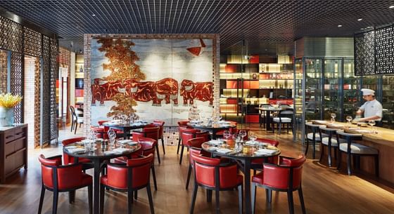Square One interior featuring round tables with red chairs, and a mural of elephants in the background at Park Hyatt Saigon
