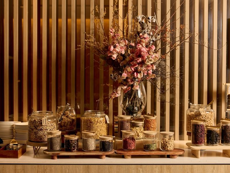 Buffet breakfast display with granola, nuts, and dried fruits in glass jars beside dried floral arrangement at Pullman East Melbourne.