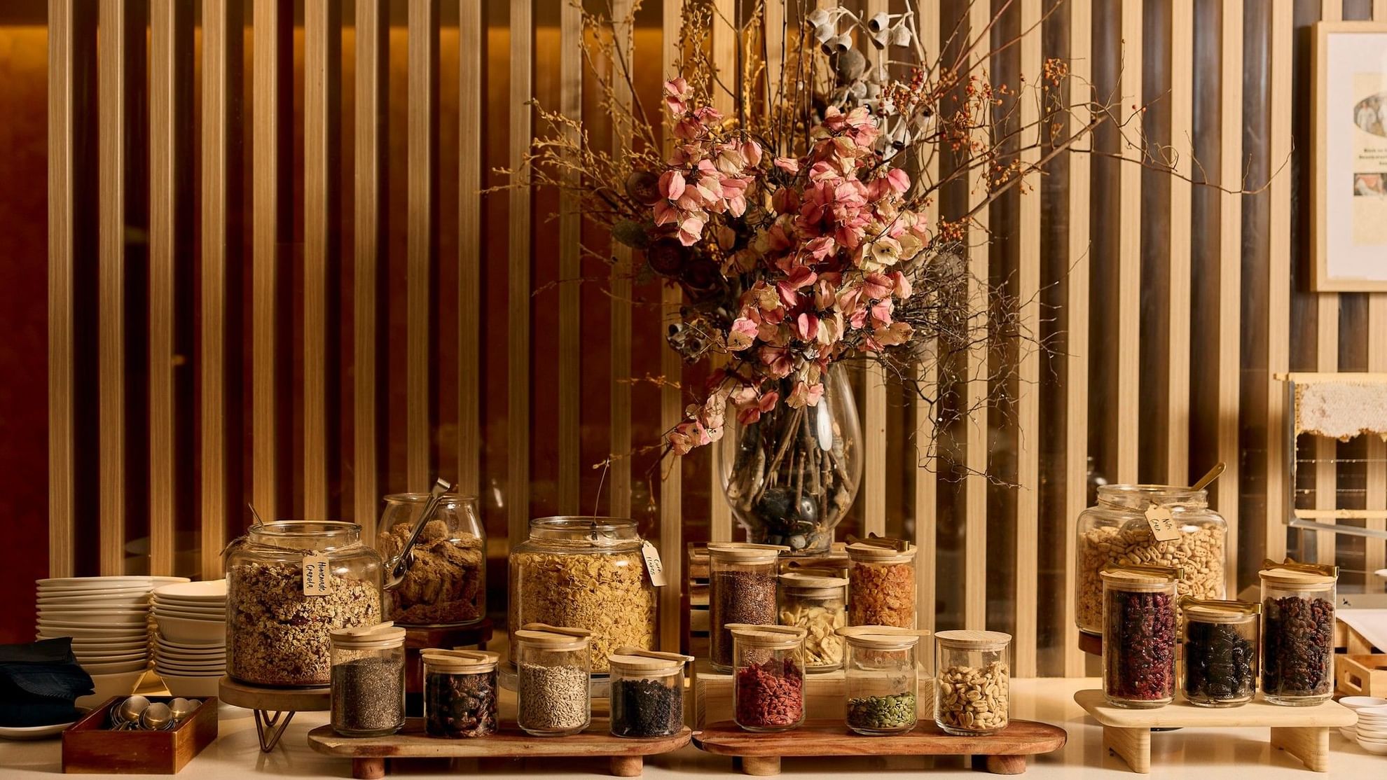 Buffet breakfast display with granola, nuts, and dried fruits in glass jars beside dried floral arrangement at Pullman East Melbourne.