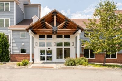 Entrance of White River Inn and Suites featuring a wooden canopy, large glass doors, and landscaped greenery