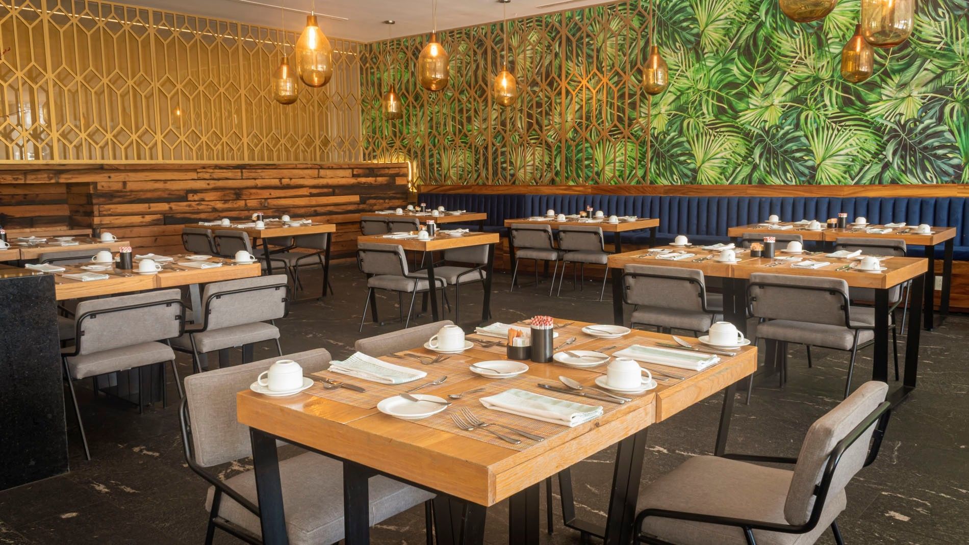 La Huerta restaurant with wooden tables and a vibrant tropical leaf wall mural at Camino Real Puebla Angelopolis