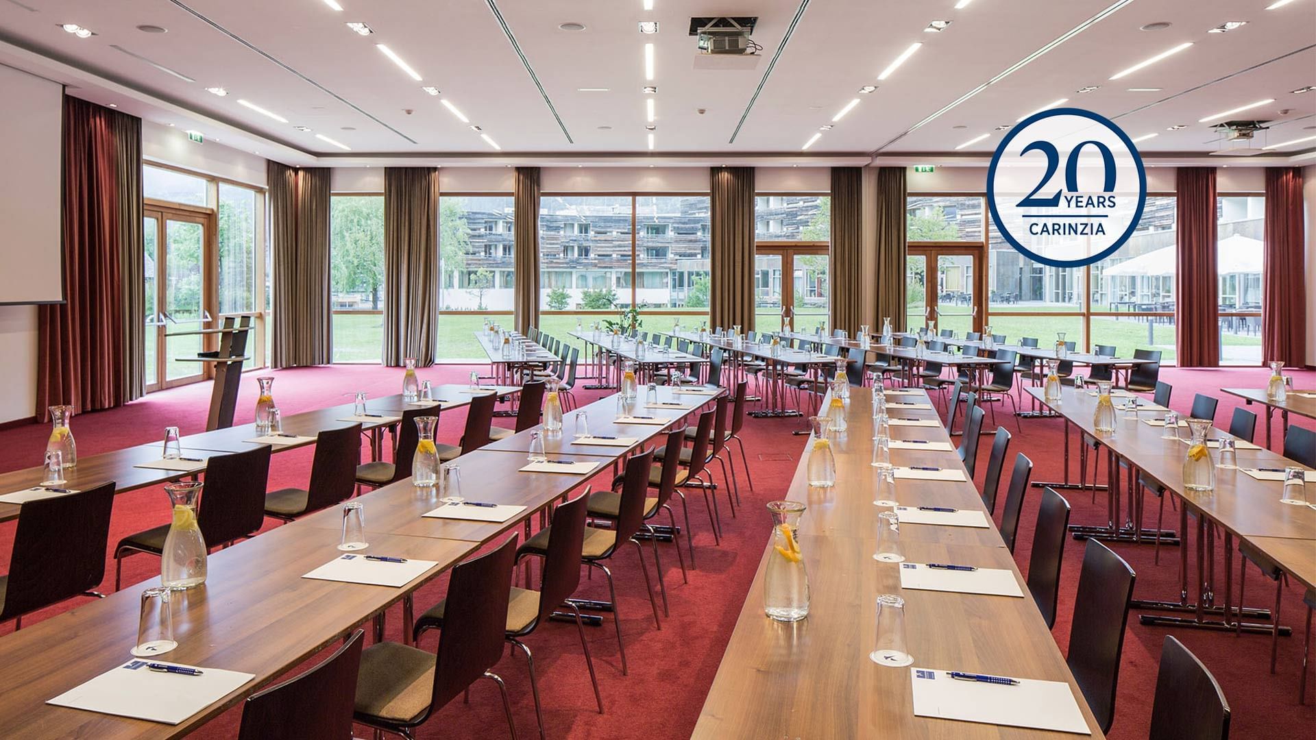 Sala riunioni con tavoli e sedie, bicchieri d'acqua, e un logo 