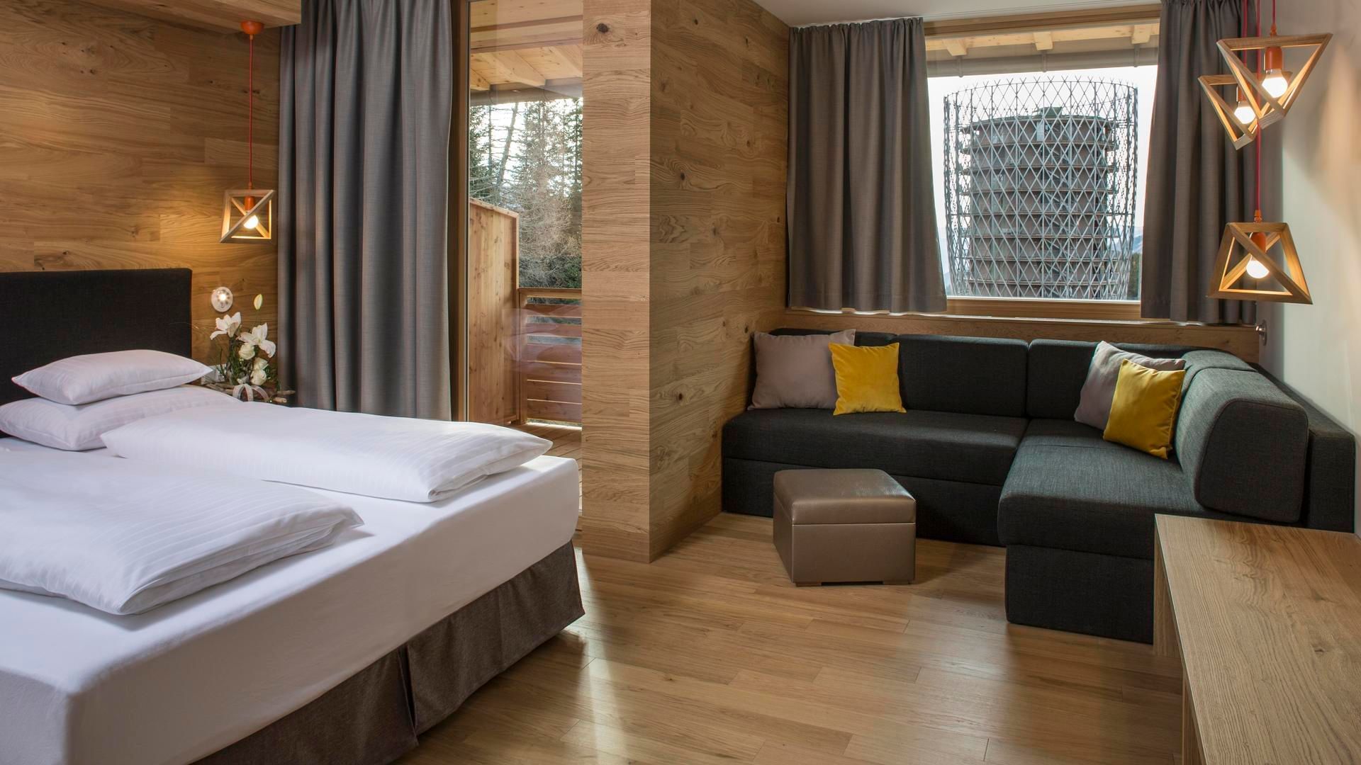 Bed with couch and wooden walls in room at Falkensteiner Hotel Cristallo