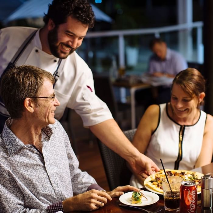 Waiter serves a plate of food to a couple at Celsius Restaurant & Bar in Mercure Hotel Townsville