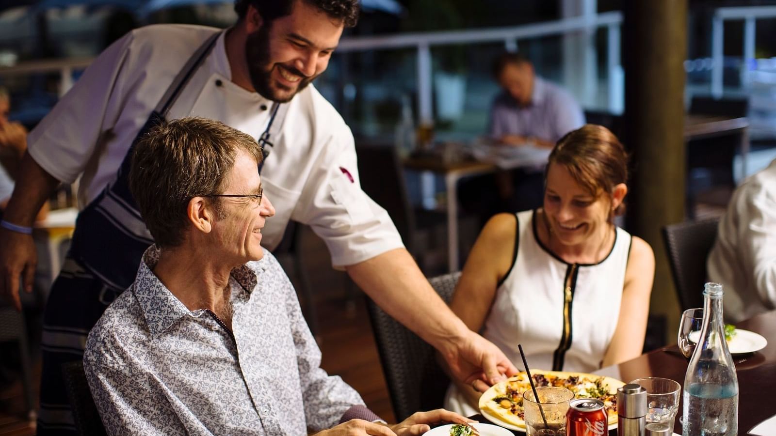 Waiter serves a plate of food to a couple at Celsius Restaurant & Bar in Mercure Hotel Townsville