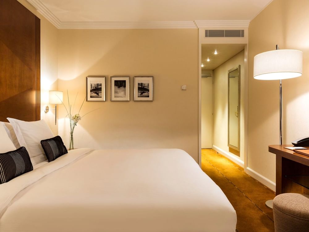 White bed by a desk under a tall lamp with framed art on the wall in Classic Room at Warwick Geneva