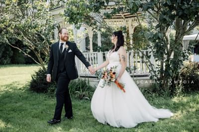 Bride and groom holding hands while walking in front of a garden gazebo outdoor at La Tourelle Hotel and Spa