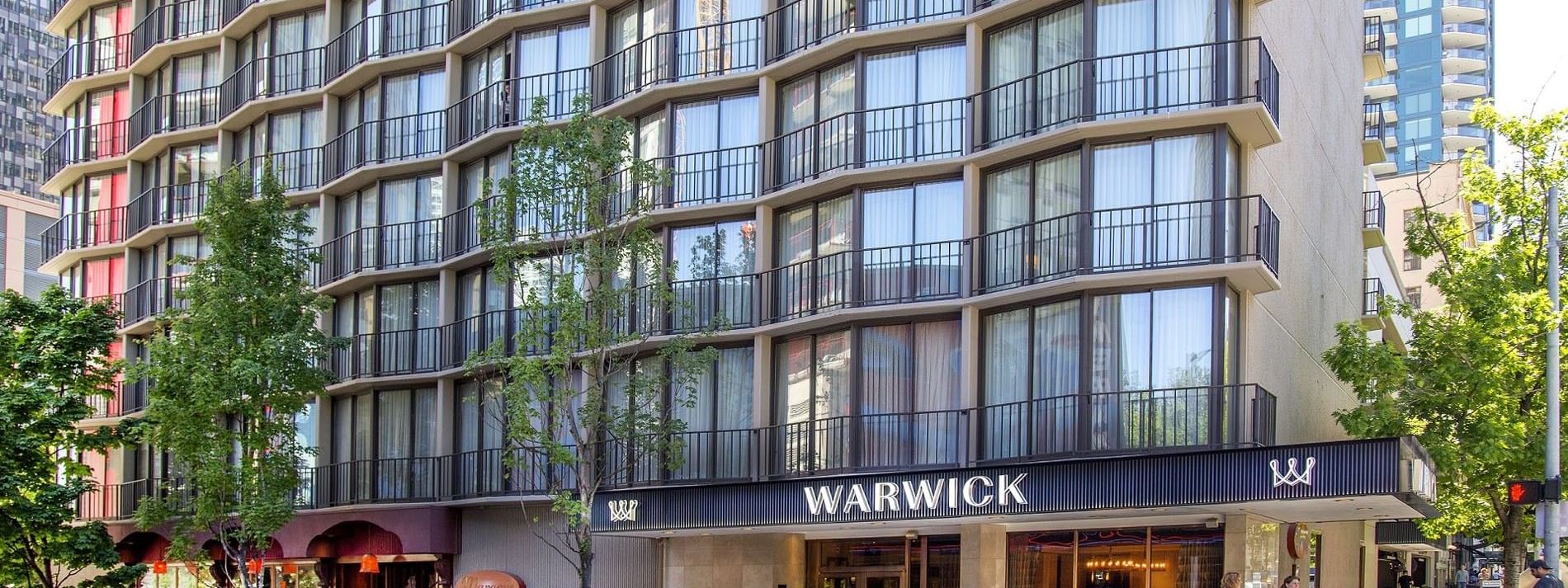 The Warwick Seattle hotel exterior, featuring yellow cabs by the entrance under tree shade