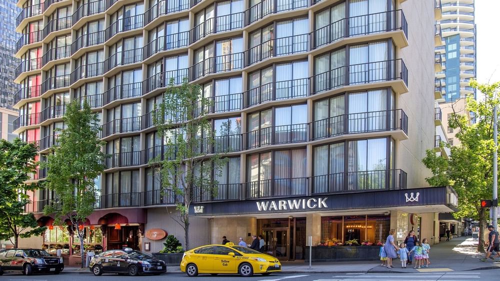 The Warwick Seattle hotel exterior, featuring yellow cabs by the entrance under tree shade