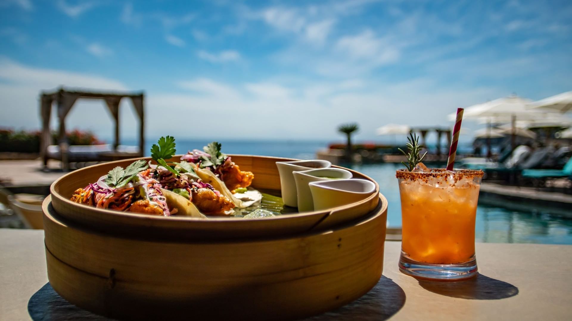 Tacos and a garnished cocktail on a table overlooking the ocean at Sirenas Restaurant in Hacienda Del Mar Los Cabos.