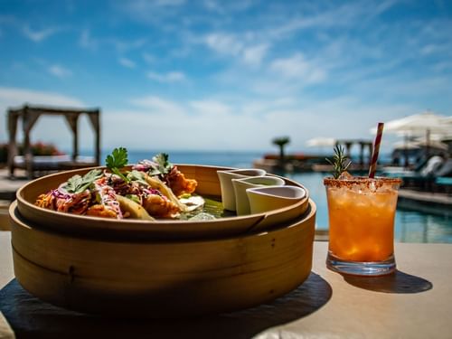 Tacos and a garnished cocktail on a table overlooking the ocean at Sirenas Restaurant in Hacienda Del Mar Los Cabos