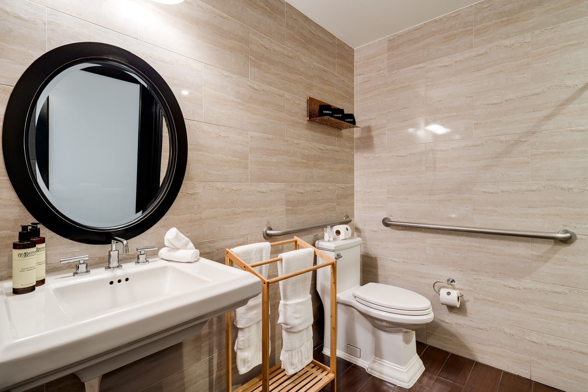 A clean bathroom with a round mirror, white sink, toilet, and towel rack.