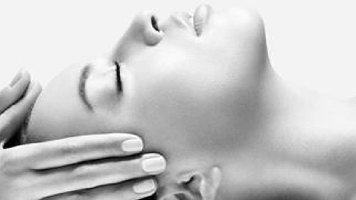 Photo en noir et blanc d'une femme recevant un massage facial avec ses yeux fermés.