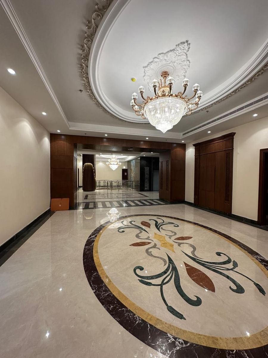 Polished marble floor with floral inlay under a crystal chandelier by wood panels at Warwick Jeddah Hotel & Spa