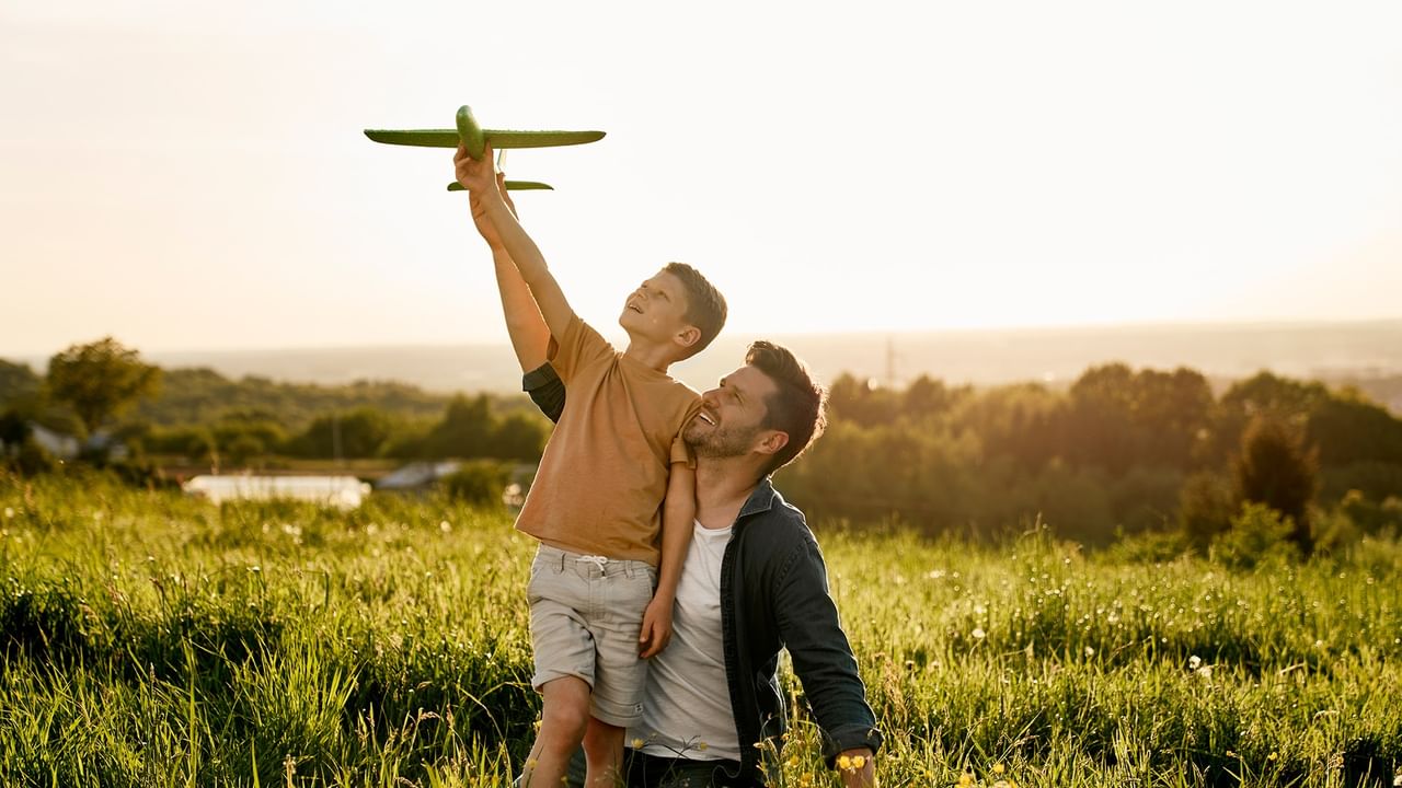 Father lifting child with toy airplane in a sunny field.