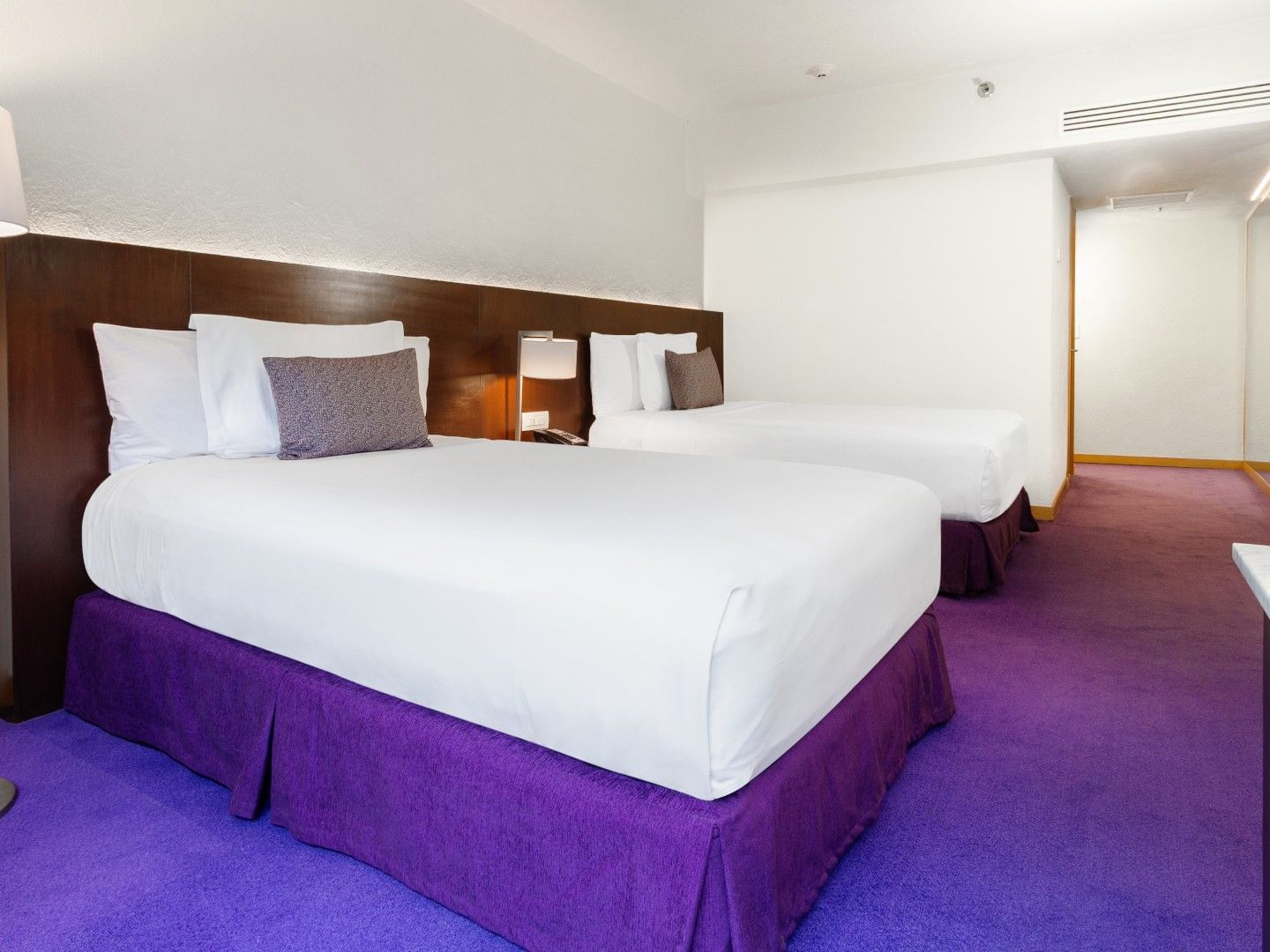 2 Double Superior Deluxe with purple bed skirts, dark wood headboard, and a long hallway at Camino Real Polanco Mexico