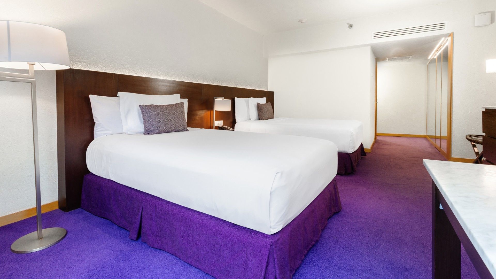 2 Double Superior Deluxe with purple bed skirts, dark wood headboard, and a long hallway at Camino Real Polanco Mexico