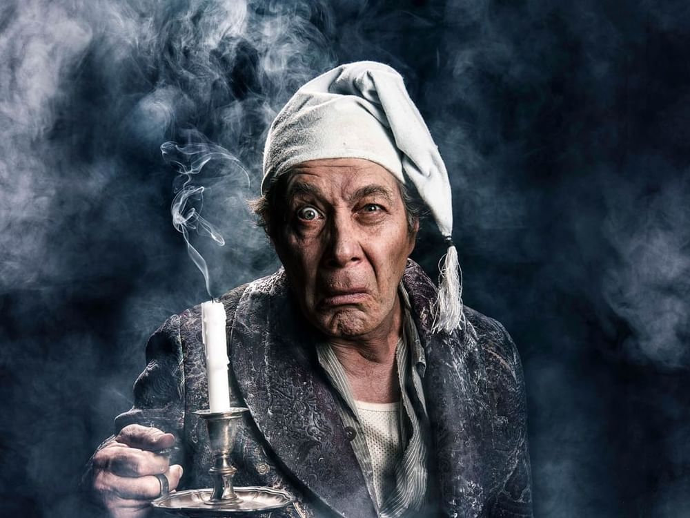 Eugene Gilfedder in old clothing holding candlestick surrounded by smoke for A Christmas Carol poster used at Sofitel Brisbane Central