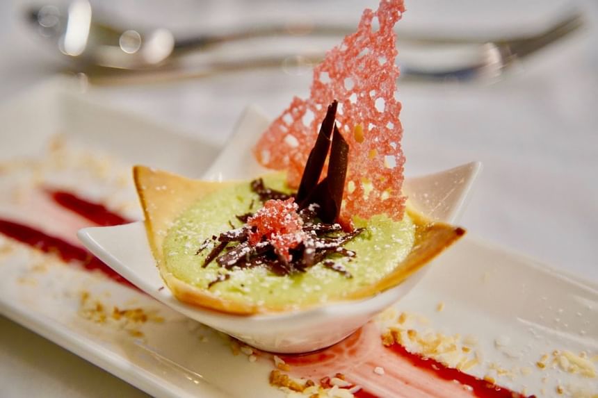 Gourmet dessert with green mousse, chocolate shavings, and a pink coral tuille garnish at The Abidah Hotel by Accra