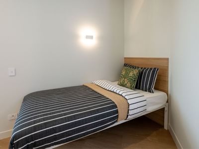 Cozy single bed with striped bedding and wall lamp in a neat room at UniLodge Brisbane City.
