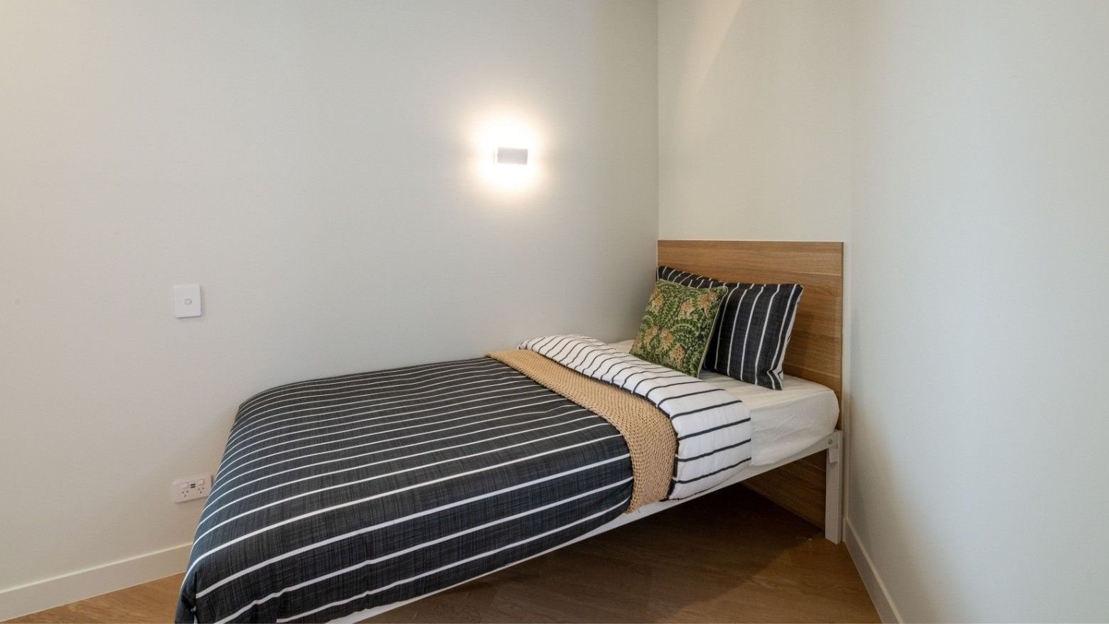 Cozy single bed with striped bedding and wall lamp in a neat room at UniLodge Brisbane City.