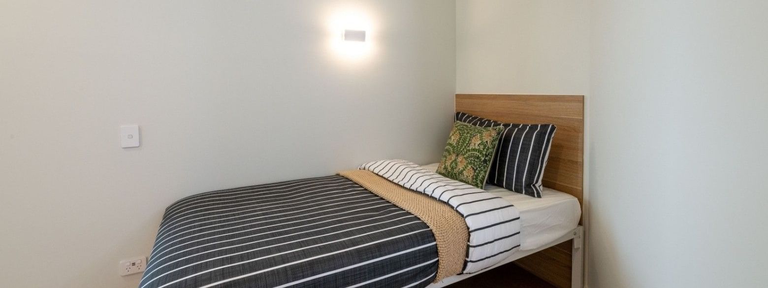 Modern single bed with striped bedding and wall light in a cozy room at UniLodge Brisbane City.